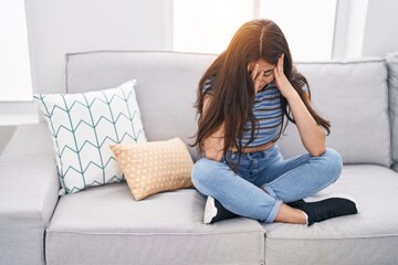 Young hispanic girl stressed sitting on sofa at home