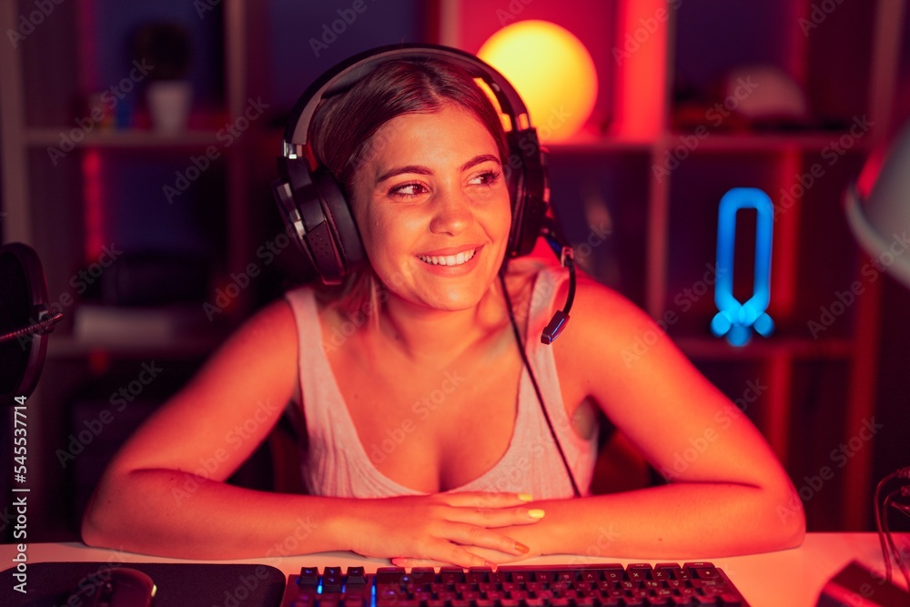 Sticker Young blonde woman playing video games wearing headphones looking away to side with smile on face, natural expression. laughing confident.