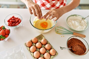 Young beautiful hispanic woman pouring egg on bowl at the kitchen