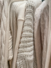 Soft cozy knit background photo of different knitted sweaters and jumpers of beige cream color.