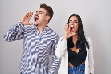 Young hispanic couple standing over white background shouting and screaming loud to side with hand on mouth. communication concept.