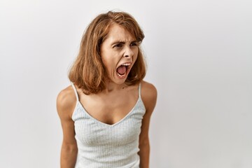 Beautiful caucasian woman standing over isolated background angry and mad screaming frustrated and...