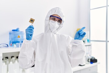 Young blonde woman holding cpu computer processor at laboratory smiling happy pointing with hand and finger to the side