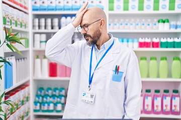 Hispanic man with tattoos working at pharmacy drugstore surprised with hand on head for mistake,...