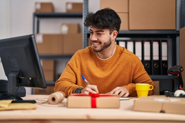 Young hispanic man ecommerce business worker writing on notebook drinking coffee at office