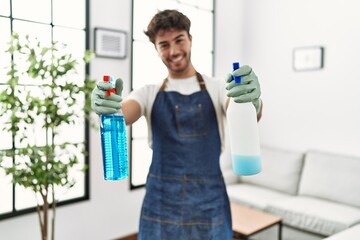 Young hispanic man doing chores holding cleaning sprayer at home