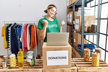 Young blonde woman wearing volunteer t shirt at donations stand very happy and excited doing winner...
