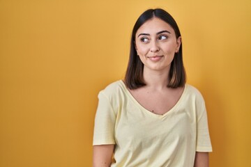 Hispanic girl wearing casual t shirt over yellow background smiling looking to the side and staring away thinking.