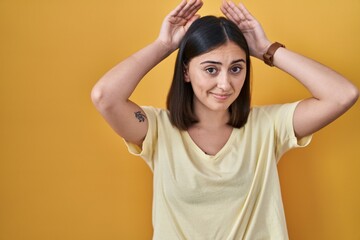 Fototapeta na wymiar Hispanic girl wearing casual t shirt over yellow background doing bunny ears gesture with hands palms looking cynical and skeptical. easter rabbit concept.