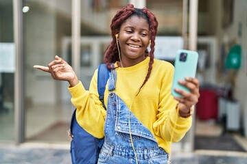 African woman doing video call with smartphone smiling happy pointing with hand and finger to the side