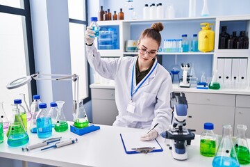Young woman scientist writing on clipboard holding test tube at laboratory