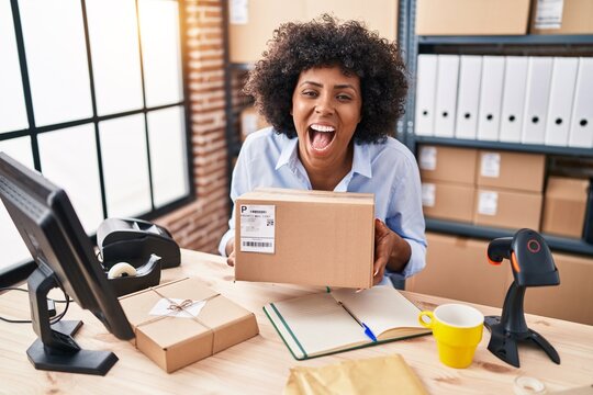 Black woman with curly hair working at small business ecommerce holding box smiling and laughing hard out loud because funny crazy joke.