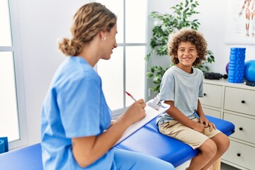 Mother and son wearing physiotherapist uniform having rehab session writing on clipboard at physiotherapy clinic