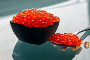 black porcelain bowl with red fish caviar close-up on a bottle-colored glass with a teaspoon filled...