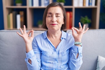 Middle age hispanic woman sitting on the sofa at home relax and smiling with eyes closed doing meditation gesture with fingers. yoga concept.