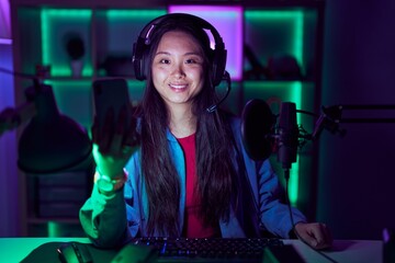 Young asian woman playing video games with smartphone with a happy and cool smile on face. lucky...