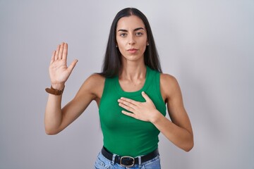 Fototapeta premium Young woman standing over isolated background swearing with hand on chest and open palm, making a loyalty promise oath