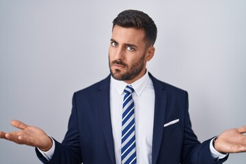 Handsome hispanic man wearing suit and tie clueless and confused with open arms, no idea concept.