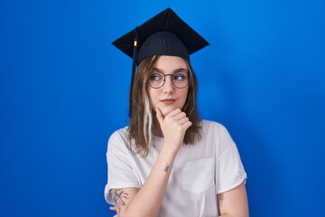 Blonde caucasian woman wearing graduation cap looking confident at the camera smiling with crossed arms and hand raised on chin. thinking positive.