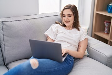 Young woman using laptop lying on sofa at home