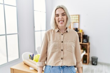 Young beautiful caucasian woman at construction office sticking tongue out happy with funny expression. emotion concept.