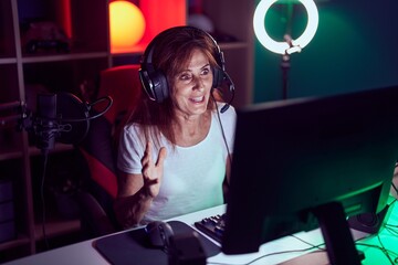 Middle age woman streamer playing video game using computer at gaming room