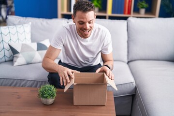 Young hispanic man smiling confident unpacking cardboard box at home
