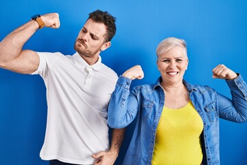 Young brazilian mother and son standing over blue background showing arms muscles smiling proud. fitness concept.