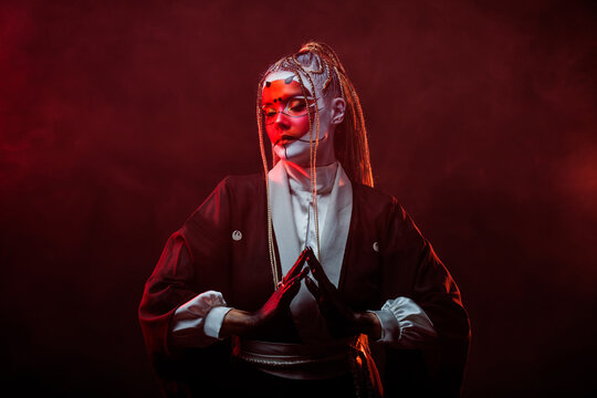 A young woman in fantastic makeup and an Asian kimono, the image of a cyber geisha. Close-up portrait, photo on a dark background with red smoke