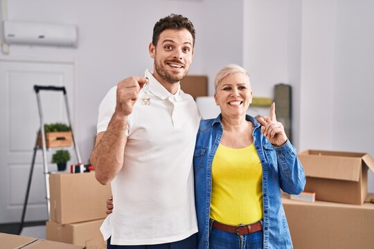 Hispanic mother and son holding keys of new home surprised with an idea or question pointing finger with happy face, number one