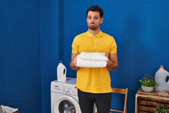 Young hispanic man holding clean towels at laundry room depressed and worry for distress, crying angry and afraid. sad expression.