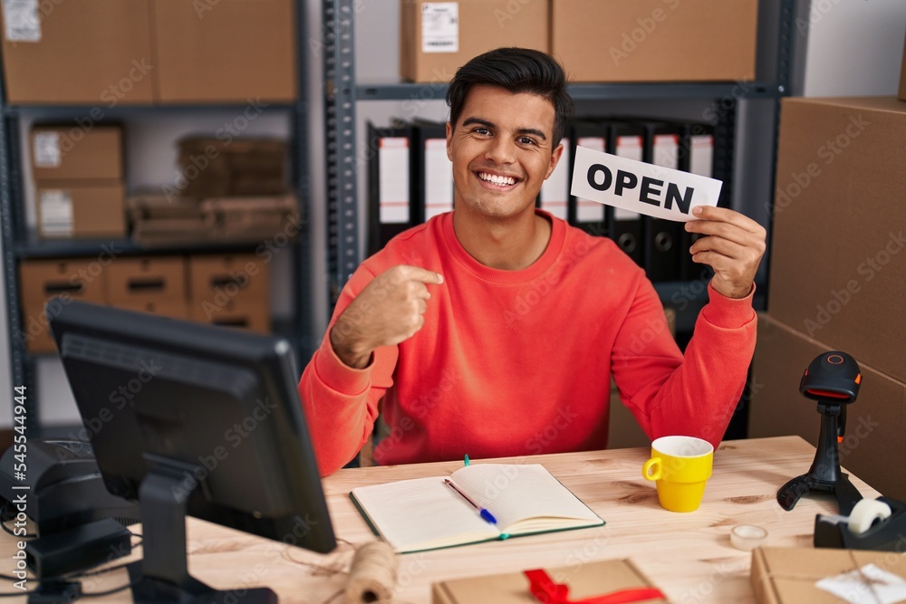 Sticker Hispanic man working at small business ecommerce holding open banner pointing finger to one self smiling happy and proud