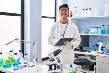 Young hispanic man scientist writing report working at laboratory