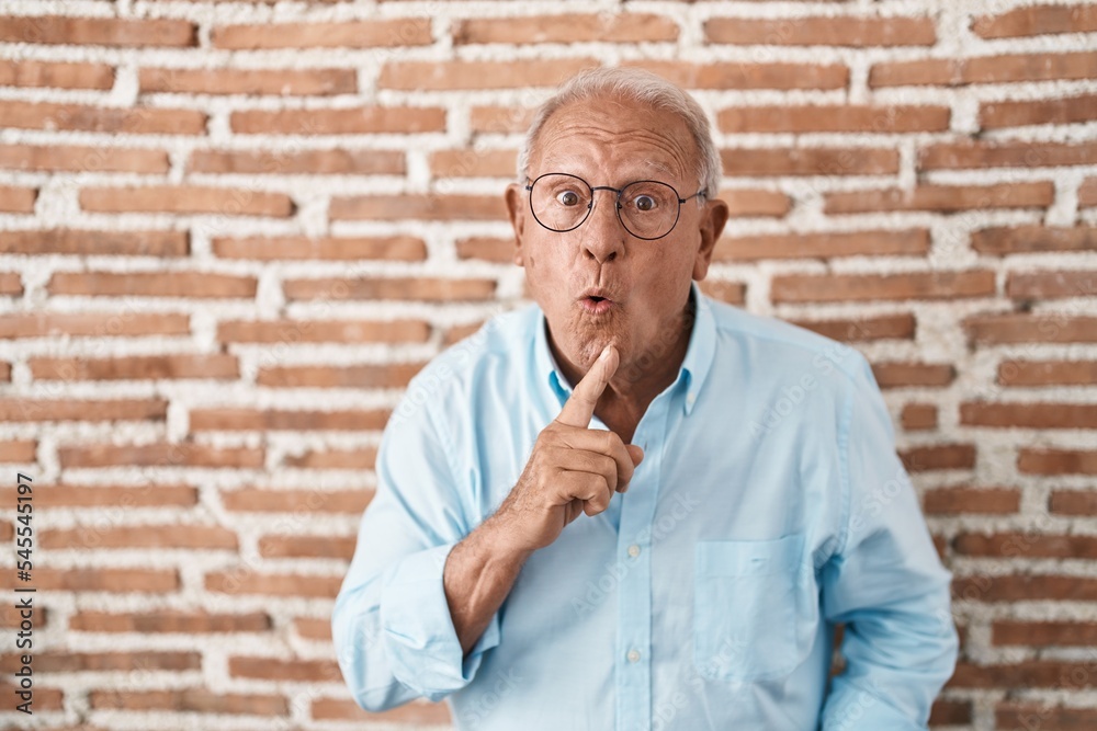 Poster Senior man with grey hair standing over bricks wall thinking concentrated about doubt with finger on chin and looking up wondering