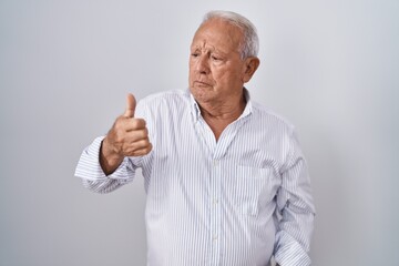 Senior man with grey hair standing over isolated background looking proud, smiling doing thumbs up gesture to the side