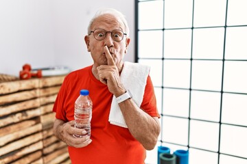 Senior man wearing sportswear and towel at the gym asking to be quiet with finger on lips. silence...