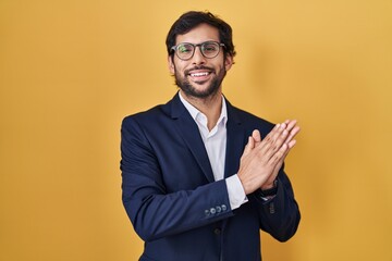 Handsome latin man standing over yellow background clapping and applauding happy and joyful, smiling proud hands together - obrazy, fototapety, plakaty