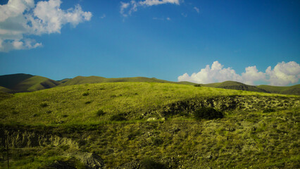 Fototapeta na wymiar Beautiful minimalistic landscape, slope with lush green grass, blue sky with fluffy clouds, wallpaper