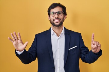 Handsome latin man standing over yellow background showing and pointing up with fingers number six while smiling confident and happy.