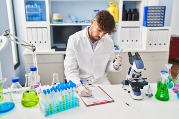 Young arab man scientist write on document analysing blood test tube at laboratory