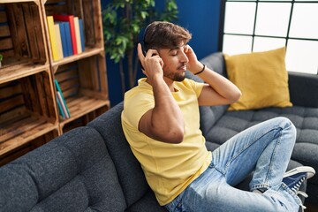 Young arab man listening to music sitting on sofa at home