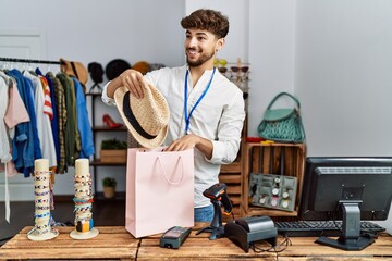Young arab man smiling confident inserting hat on shopping bag at clothing store