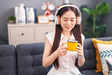 Young chinese woman listening to music drinking coffee at home