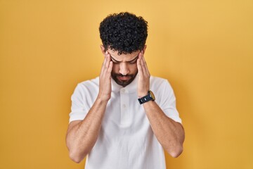 Arab man standing over yellow background with hand on head, headache because stress. suffering migraine.