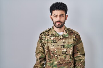 Arab man wearing camouflage army uniform relaxed with serious expression on face. simple and natural looking at the camera.