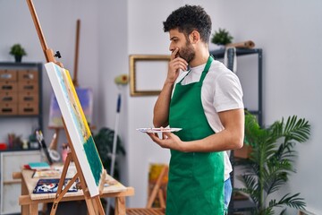 Young arab man artist looking drawi with doubt expression at art studio