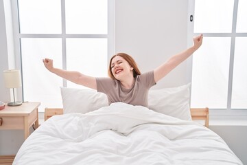 Young redhead woman waking up stretching arms at bedroom