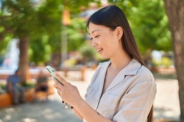 Chinese woman smiling confident using smartphone at park