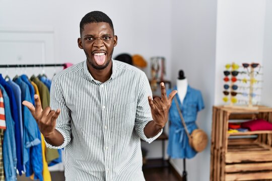 Young african american man working as manager at retail boutique shouting with crazy expression doing rock symbol with hands up. music star. heavy concept.