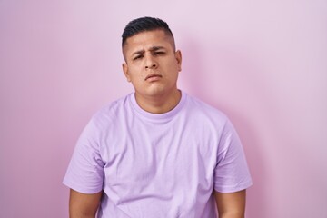 Young hispanic man standing over pink background looking sleepy and tired, exhausted for fatigue and hangover, lazy eyes in the morning.